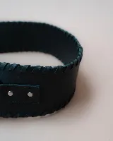 Faja de cuero negro con diseño ancho y costuras decorativas en los bordes. Presenta una hebilla metálica circular plateada en el centro y un diseño asimétrico en la parte frontal.
