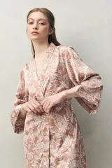 Bata de pijama color rosado con estampado floral en blanco, de silueta relajada, tipo kimono, con cruce frontal y lazo regulable en la cintura. Tiene mangas amplias y largo por encima de la rodilla.