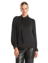 Blusa negra de acabado satinado con cuello alto fruncido, detalle de lazo para anudar y cierre lateral con botones. Presenta mangas largas estilo balloon con puños ajustados.
