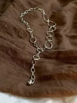 Collar de cadena con eslabones irregulares de diseño artesanal, con cierre frontal tipo barra y aro. La pieza permite diversas formas de uso, incluyendo como collar, pulsera o accesorio de espalda.
