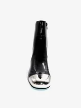 Bota corta de cuero negro con acabado brillante, tacón de bloque y puntera metálica plateada. Cuenta con cierre lateral.