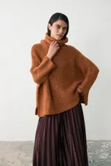 Sweater tipo poncho de tejido de punto grueso en color ocre, con cuello alto holgado y diseño de corte amplio con aberturas laterales en el ruedo.