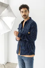 Sobrecamisa de tejido polar con estampado abstracto en tonos rojizos y azul marino. Presenta cuello clásico, cierre frontal con botones a presión, dos bolsillos frontales con solapa en el pecho y un parche decorativo.