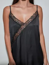 Vestido midi negro de satén con detalles de encaje en el escote, el ruedo y una aplicación diagonal que cruza el diseño. Cuenta con tirantes finos y un corte fluido.