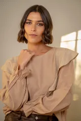 Blusa blanca de algodón con cuello redondo, mangas largas con puños elásticos y volados decorativos en los hombros.