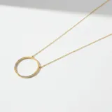 Collar de cadena fina con dije circular, elaborado en plata 925 con baño de oro. El dije presenta un diseño minimalista con incrustaciones de circonias en dos secciones opuestas del círculo.