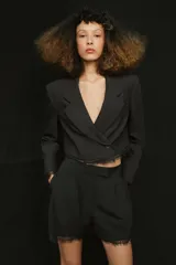 Blazer corto de corte recto con cuello solapa, manga larga y cierre frontal con un botón. Presenta detalles de encaje a tono en el ruedo y en los puños, con forro interior.