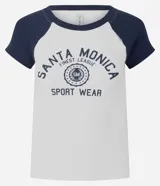 Remera de estilo college con cuerpo blanco y mangas raglán cortas en color azul marino. Presenta cuello redondo y estampa frontal con diseño gráfico deportivo de Santa Monica.