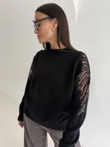 Sweater negro de tejido de punto con cuello redondo y mangas largas. Presenta detalles de transparencias y apliques bordados con pedrería en la parte superior de las mangas.