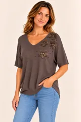 Remera de punto color marrón chocolate, de manga corta y escote en V, con apliques de flores de tela y cuentas metálicas en el hombro y pecho izquierdo.