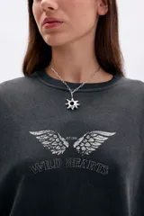 Buzo oversize negro con efecto desgastado, cuello redondo y estampado frontal de alas con la frase "Wild Hearts".