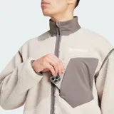 Chaqueta de felpa peluda Adidas Terrex Xploric High Pile de corte holgado, color beige claro con detalles en marrón oscuro en el cuello alto, los ribetes, el cierre frontal y el bolsillo del pecho. Cuenta con bolsillos laterales y un bolsillo con cierre en el pecho.
