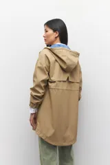 Piloto verde militar de manga larga con capucha y forro de color amarillo. Cuenta con dos bolsillos laterales con solapa, cordones ajustables, elástico en los puños, cierre y botones metálicos.