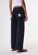 Jean de corte recto y tiro bajo, color negro, con diseño de estrellas blancas estampadas en los bolsillos traseros y detalles de tachas metálicas en los laterales.
