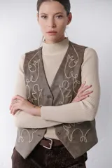 Chaleco marrón de simil cuero con bordado en color crema, cuello en V y cierre frontal con botones.