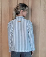 Camisa de manga larga con estampado de rayas verticales en tonos crudo y beige. Presenta cuello alto con volados, cierre frontal con botones dobles y puños con volados.