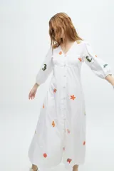 Vestido largo blanco de algodón con bordados de motivos marinos en tonos naranja, verde y azul. Tiene escote en V, mangas 3/4 abullonadas y cierre frontal con botones.