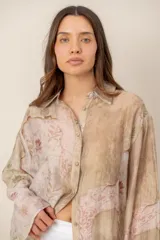 Camisa beige de manga larga con estampado botánico y floral, confeccionada en tejido liviano y traslúcido, con cuello camisero y cierre frontal de botones.