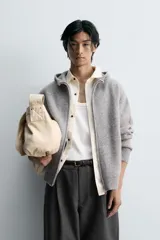 Chaqueta de punto con capucha, corte relajado, manga larga, bolsillos laterales y cierre frontal con cremallera. Presenta acabados en rib en puños y bajo.