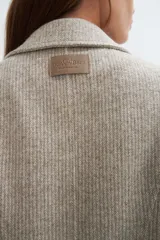 Saco corto entallado de lana fina, con cuello solapa, manga larga y cierre frontal con botones. Presenta un diseño clásico con textura de espiga en tonos tierra.