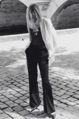 Pantalón negro de tiro alto con pierna ancha y pliegues marcados al frente. Presenta cierre frontal y un botón decorativo dorado en la pretina.