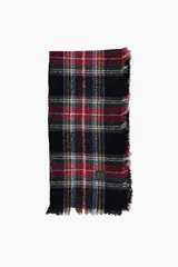 Pashmina de formato cuadrado con diseño de cuadros escoceses en tonos negro, rojo, verde y amarillo. Presenta terminaciones con flecos en sus bordes y una pequeña etiqueta decorativa.