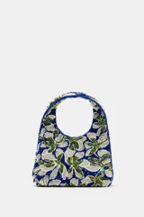 Bolso de mano mini con diseño floral bordado en abalorios y lentejuelas en tonos azul, verde y blanco. Cuenta con asa integrada, forro interior con bolsillo y cierre mediante botón imantado.