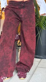 Pantalón de denim con efecto lavado, de corte recto y tiro bajo. Cuenta con cordones ajustables en los tobillos para modificar la silueta y cierre frontal con botón y cremallera.