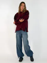 Sweater de punto color bordó, con cuello redondo, mangas largas abullonadas y detalle de flecos en las costuras de los hombros.