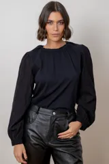 Remera negra con cuerpo de algodón y mangas largas de tela con textura calada, cuello redondo con elástico y frunce, y puños elásticos.