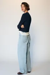 Jeans de tiro medio con diseño wide leg y pernera ancha. Presenta cinco bolsillos, cierre frontal con cremallera y botón, y detalle de raya planchada en el delantero y la espalda.