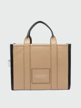 Cartera tipo tote bag Marc Jacobs modelo The Medium Leather Tote Bag, color marrón tostado con detalles en negro, confeccionada en cuero con las inscripciones "THE TOTE BAG" y "MARC JACOBS" estampadas en el frente. Cuenta con asas superiores y correa ajustable y desmontable para el hombro.