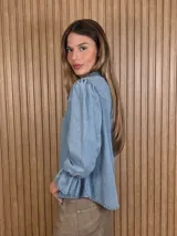 Blusa color lila con estampado vertical de ramas y hojas blancas, cuello alto con volados y escote en V. Presenta mangas largas abullonadas con puños elastizados.