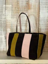 Bolso shopper de cuero y gamuza con diseño de franjas verticales en colores negro, rosado y mostaza. Cuenta con dos asas de hombro y cierre superior.