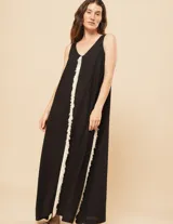 Vestido largo negro de lino, con escote en V tanto en la parte delantera como en la espalda, y flecos de algodón blancos en los laterales.