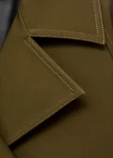 Chaqueta corta de doble botonadura en color verde militar, con cuello de solapa, bolsillos laterales, trabillas en los hombros y mangas largas con puños abotonados.