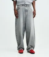 Pantalón de jean estilo baggy balloon, de corte holgado con volumen en las piernas y cintura fija con trabillas. Presenta costuras a contratono y detalle de cadena metálica lateral.