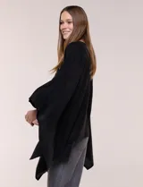 Poncho de calce holgado color marrón, confeccionado en tejido fino de punto suave, con cuello redondo y diseño de caídas laterales amplias de ruedo asimétrico.
