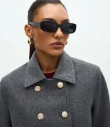 Saco corto de corte regular confeccionado en polivelour gris, con cuello inglés, cierre frontal de doble abotonadura con botones dorados y mangas largas con detalle de trabas en los puños.