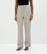 Pantalón de sastrería marca Cortelle, de corte recto y color beige. Presenta pliegues delanteros, cintura con trabillas, cierre frontal y bolsillos traseros embutidos.