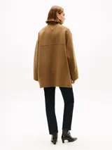 Abrigo de corte oversize confeccionado en mezcla de lana de doble cara, color marrón. Presenta cuello chimenea, cierre frontal con un botón visible y otro oculto, y dos bolsillos delanteros de parche.