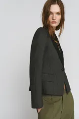 Blazer Zara Woman Collection de corte estructurado en tejido de espiga gris, con solapas de muesca en contraste color negro. Presenta cierre frontal con un botón, mangas largas y bolsillos delanteros con solapa.