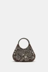 Bolso de mano mini con cuerpo de efecto aterciopelado en color marrón, adornado con abalorios y lentejuelas que forman un estampado floral. Cuenta con doble asa de mano rígida decorada con cuentas y cierre magnético.