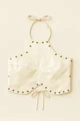Top halter de cuero ovino color off-white, con diseño panelado y tachas color oro viejo. Se ajusta en el cuello con lazo y en la espalda con tres tiras ajustables.