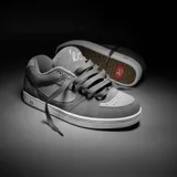 Zapatillas grises de skate con detalles en gris claro, confeccionadas en gamuza, con suela blanca y logo de la marca en el lateral.
