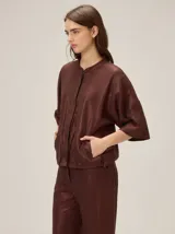 Chaqueta de lino y rayón color bordó con acabado metalizado, cuello mao, mangas cortas amplias, bolsillos laterales y cordón ajustable en la cintura.