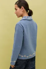 Chaqueta de lana merino hervida en color marrón, con diseño estructurado y cuello amplio. Presenta detalles de bordado artesanal en contraste color mostaza a lo largo del frente, cuello y puños, junto con botones forrados en la misma tela.