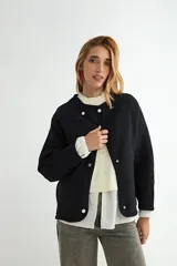 Campera corta de paño color negro, con cuello redondo, mangas largas y cierre frontal con botones a presión metálicos.