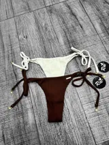 Bombacha de bikini con textura acanalada, tiras laterales ajustables para atar y detalles de dijes dorados en los extremos.