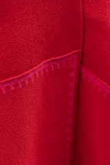 Ruana de tejido de punto color rojo, con diseño envolvente y bordes decorados con costuras a contraste en tono fucsia.